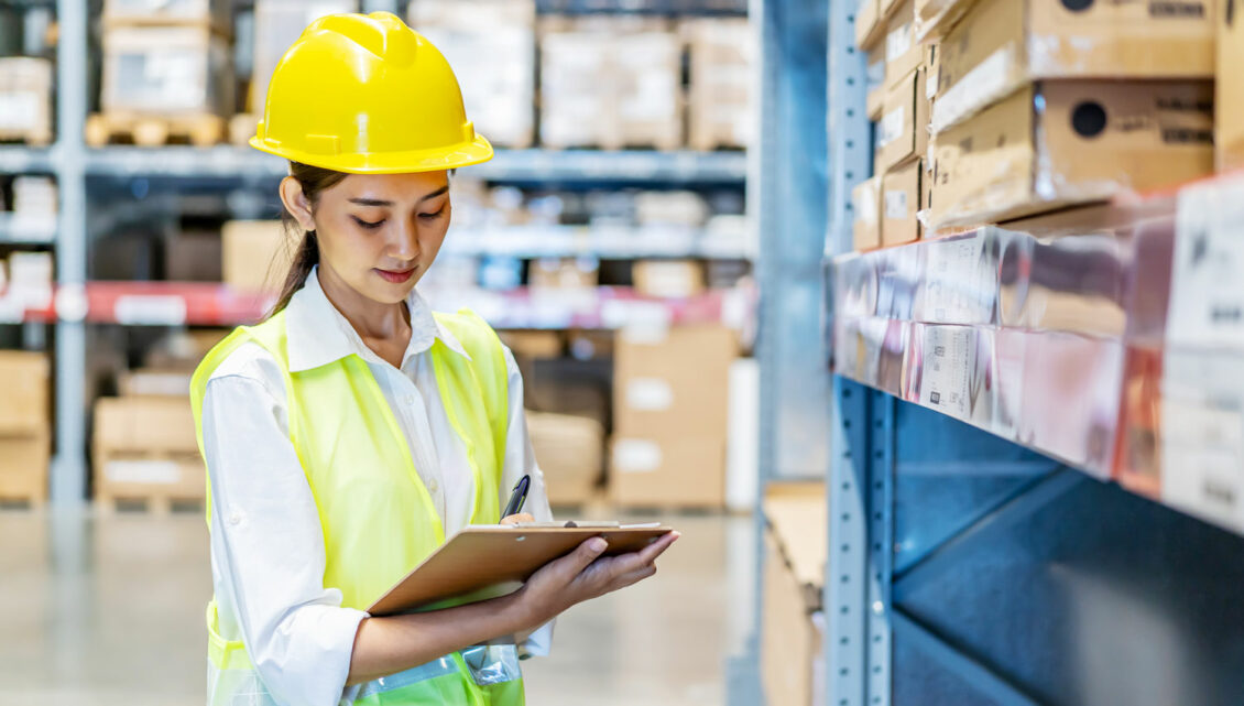 A woman wearing a hard hat looks at stock information on a tablet device