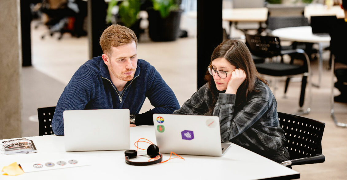 Two data scientists working on laptops in an office