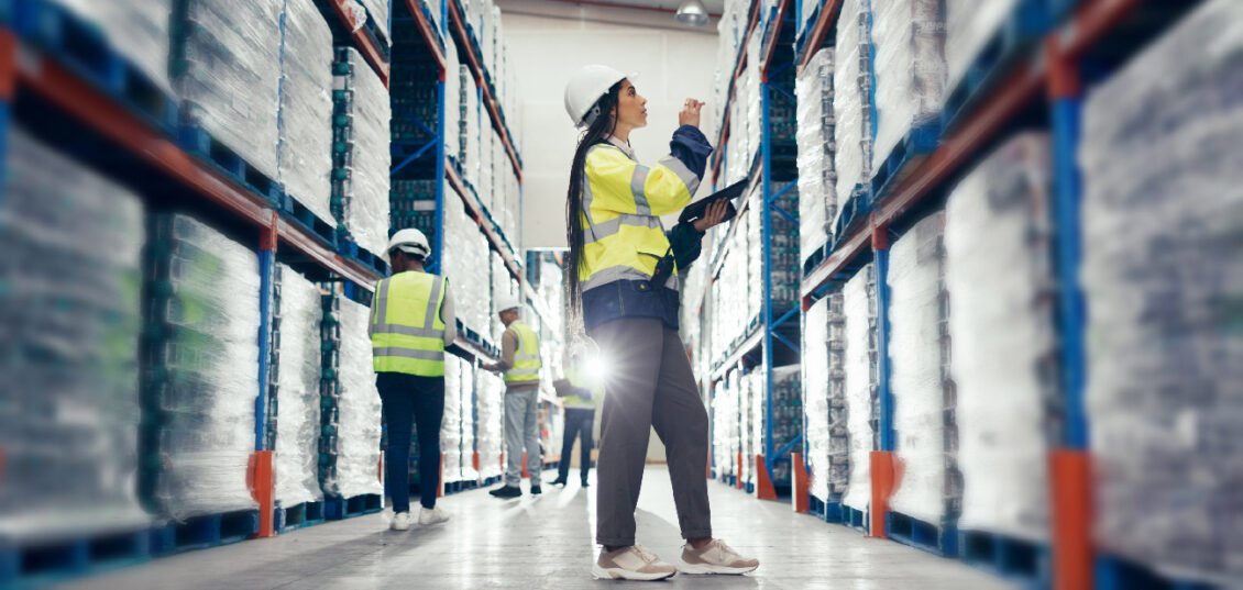 Workers in a warehouse wearing hard hats and hi vis jackets.
